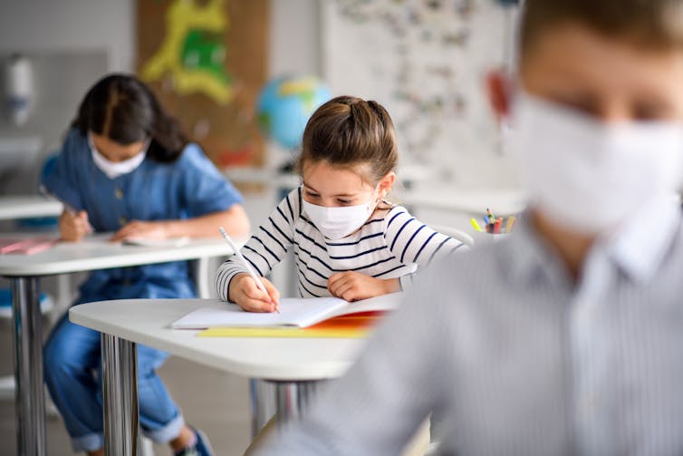 Children wearing masks write during class.