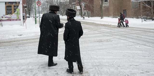 Two Hasidic men converse on a street.