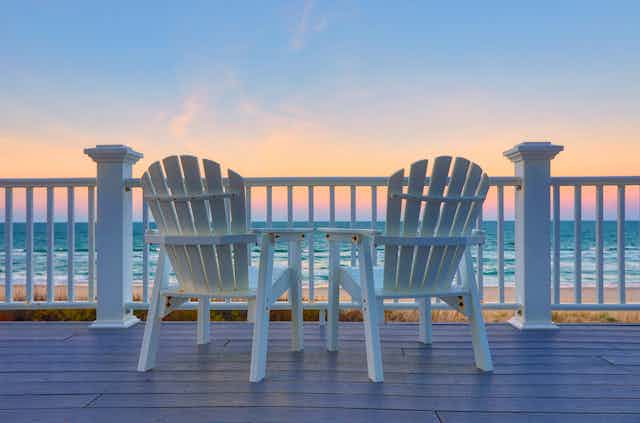 Two empty white adirondack chairs facing the ocean