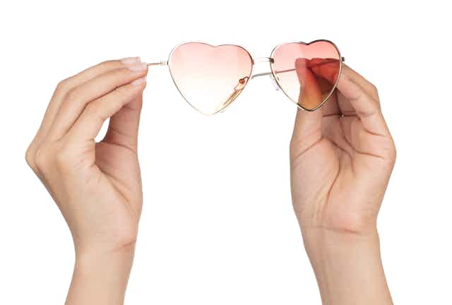 Hands holding a pair of pink-tinted heart-shaped glasses