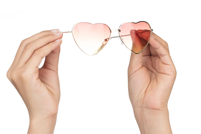 Hands holding a pair of pink-tinted heart-shaped glasses