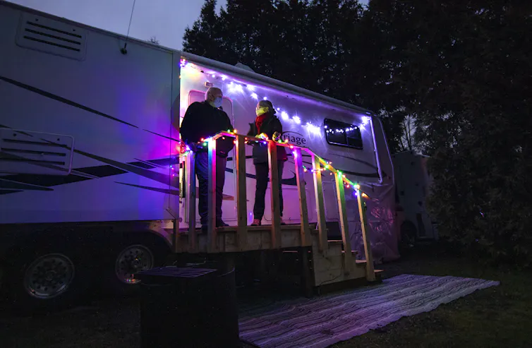 Un couple debout sur les marches de leur caravane au crépuscule, avec des lumières décoratives