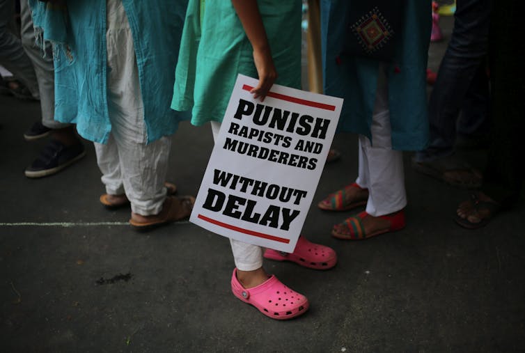 A woman carries a placard which reads: punish rapists and murderers without delay.