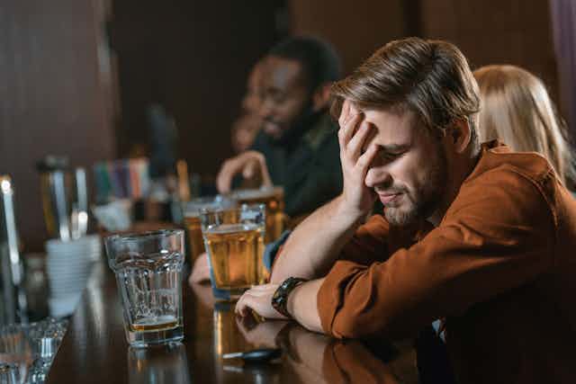 Person drinking at bar with head in hands looking confused