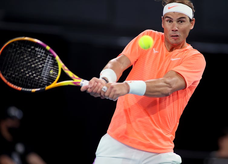 Rafael Nadal holding a tennis racket and about to hit a ball.