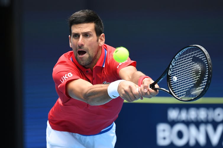 Novak Djokovic stretching with both hands on the racket about to hit the tennis ball.