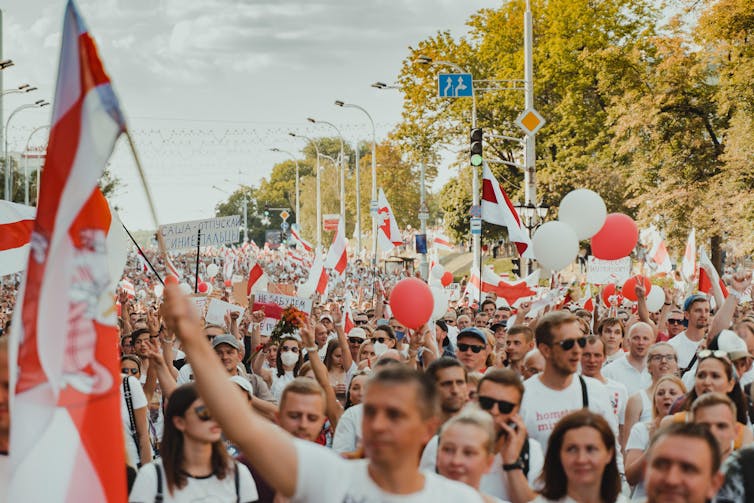 People protesting in streets in Belarus holding red and white flags.