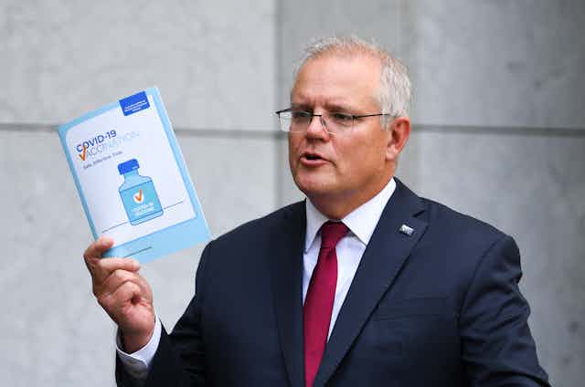 Scott Morrison, holding a COVID-19 vaccination pamphlet