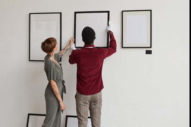 Woman touches frame while man holds it in place against gallery wall