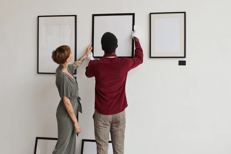 Woman touches frame while man holds it in place against gallery wall
