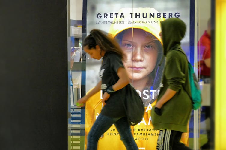 Young people walk past a sign advertising Greta Thunberg's book in Italy.