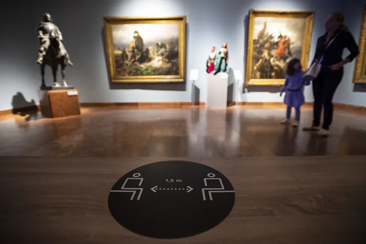 A mother and child at an art gallery, with a social distancing warning sign in the foreground.