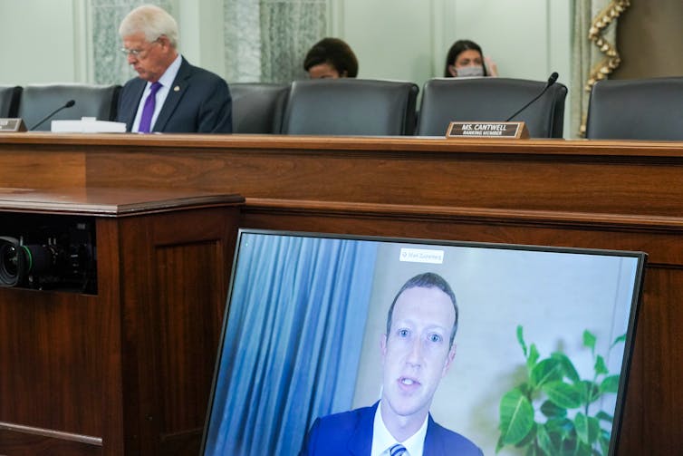 A screen showing Mark Zuckerberg lies against a desk in the US senate for a hearing