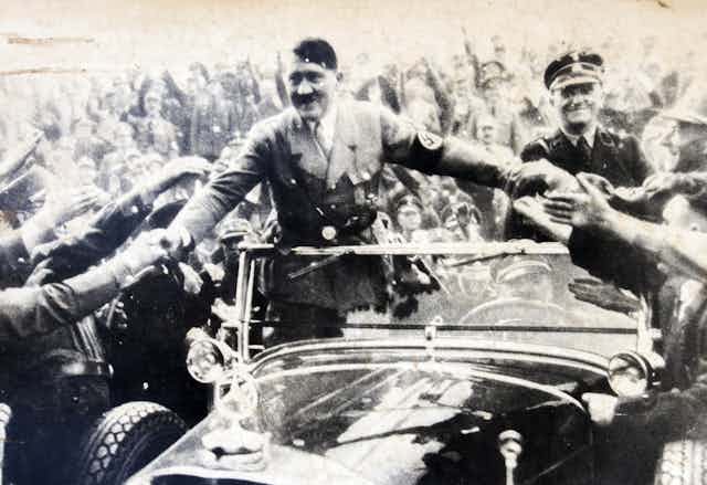Adolf Hitler riding in an open car greeting supporters.