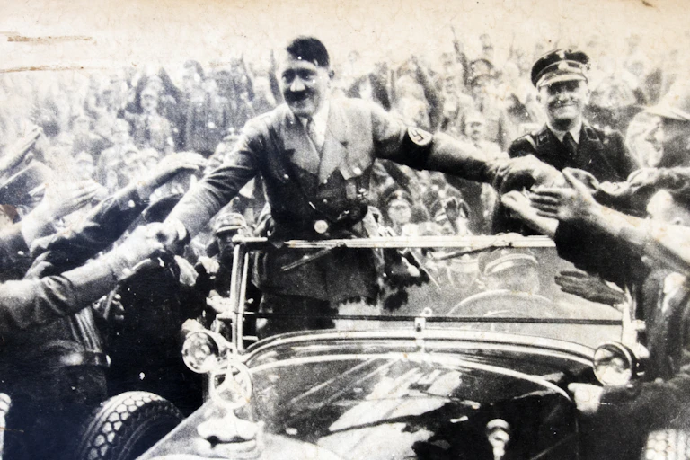 Adolf Hitler riding in an open car greeting supporters.