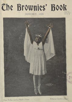A smiling girl dressed in white raises her arms and stands en pointe.