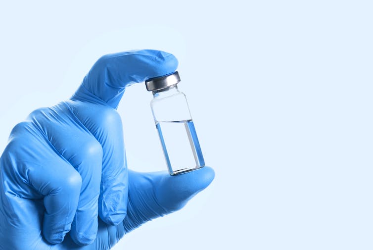 A gloved hand holding half a vial of vaccine