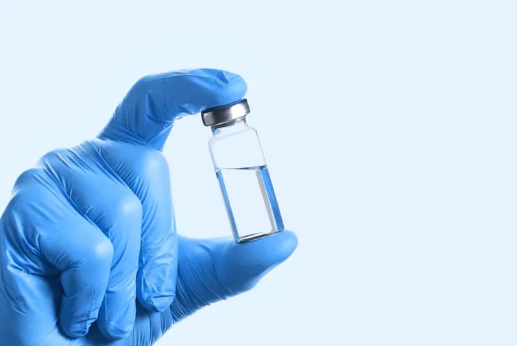 A gloved hand holding half a vial of vaccine