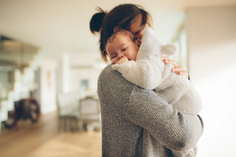 Mother holding baby inside house.