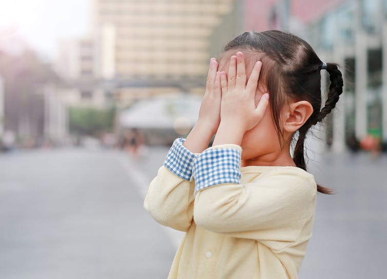 Young girl covering her eyes outside