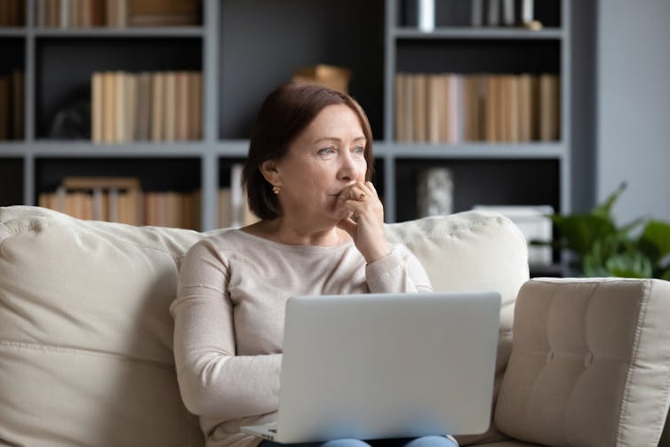 Middle-aged woman sitting on sofa with laptop looking concerned