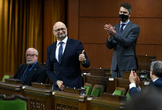 Minister of Justice David Lametti standing, giving thumbs up, as colleagues clap.
