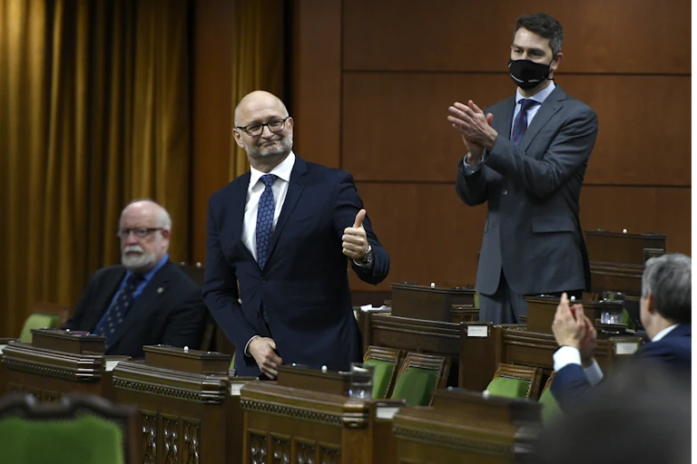 Minister of Justice David Lametti standing, giving thumbs up, as colleagues clap.