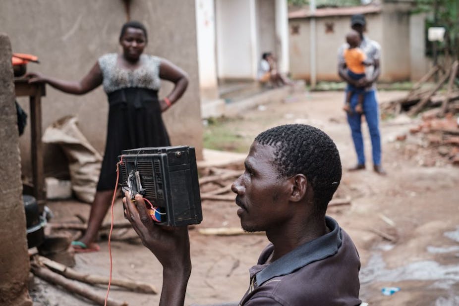 A man holds his radio close to his ears while a woman stands nearby.