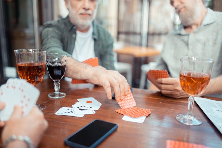 Bearded grey-haired men drinking alcohol and playing cards at a table with drinks