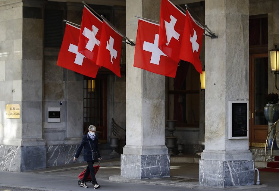 Une femme passe devant les drapeaux suisses en portant un masque de protection