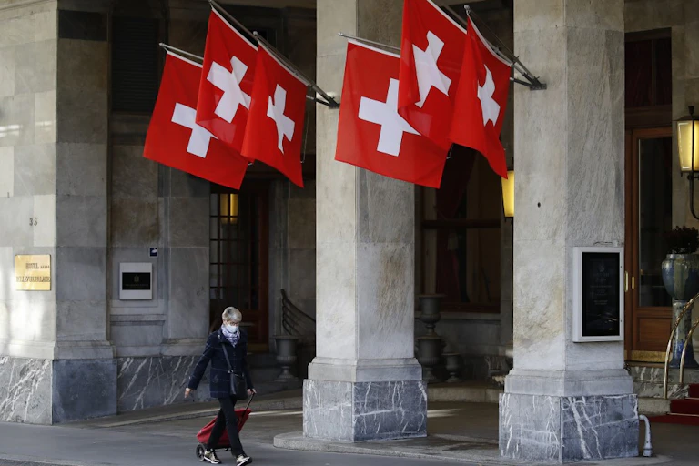 Une femme passe devant les drapeaux suisses en portant un masque de protection