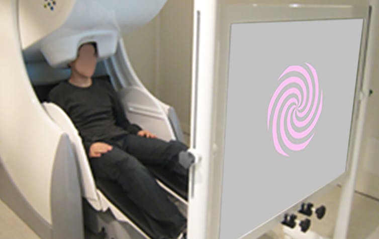 Person seated in MEG machine looking at screen with color projection