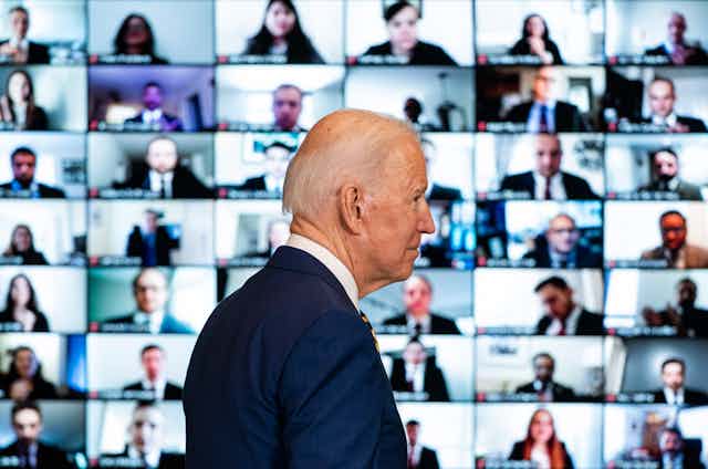 US president Joe Biden walks past a bank of screens showing a Zoom meeting with state department staff, February 4, 2021.