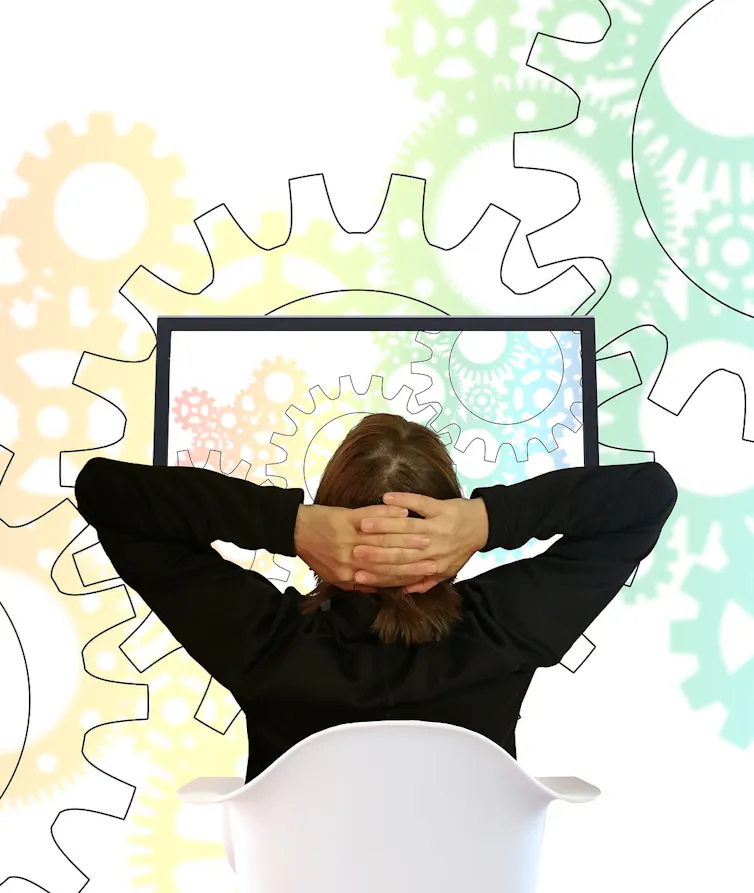 A man sits in front of a desktop computer with a mural of gears in the background.