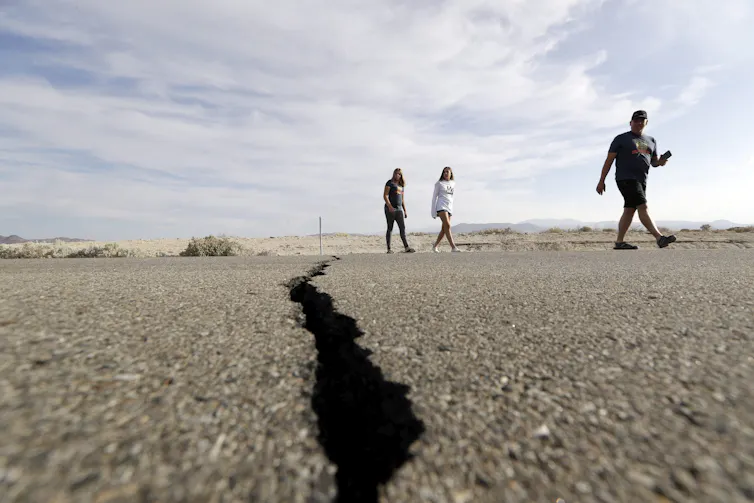 Visitors cross a highway with a large crack caused by an earthquake.