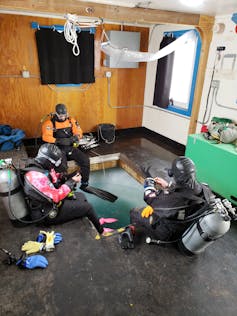 SCUBA divers sit around a square hole cut in Antarctic ice
