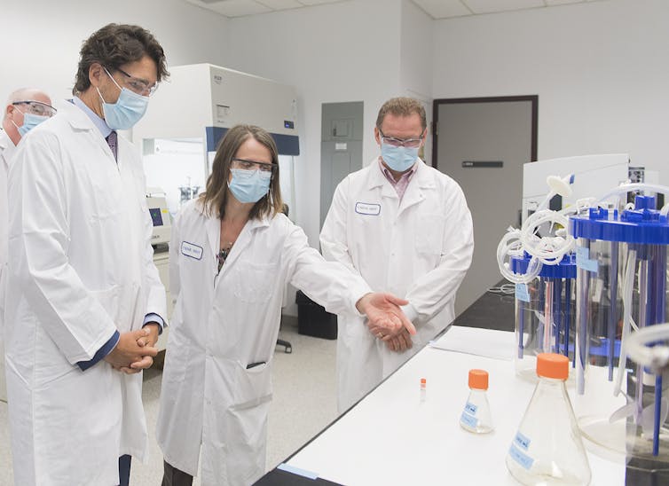 Trudeau and two scientists, all in white lab coats and face masks, in a lab