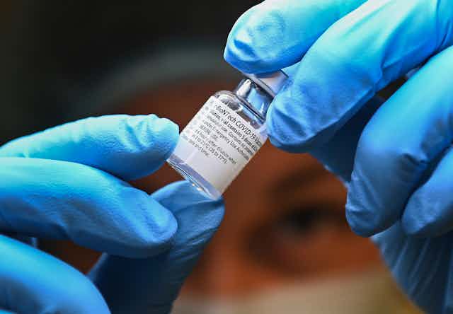 Close-up of gloved hands holding a vial of vaccine