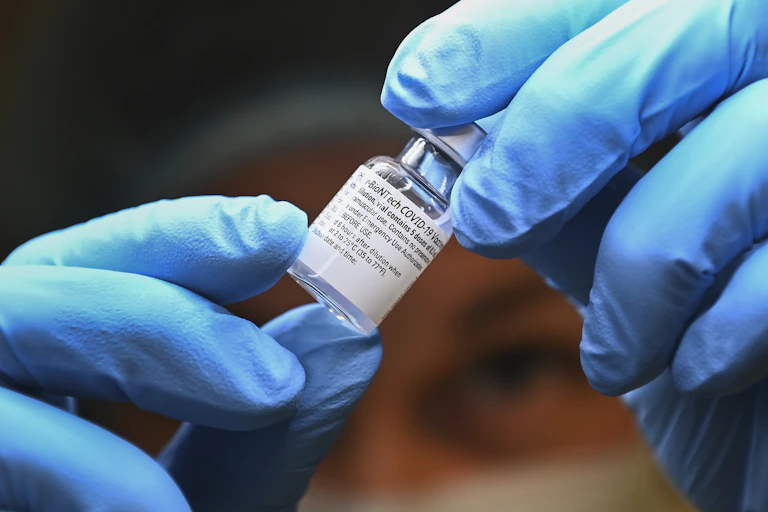 Close-up of gloved hands holding a vial of vaccine