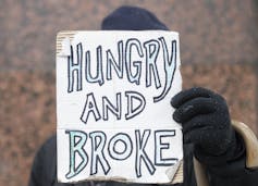 A homeless man holds up a sign reading Homeless and Broke.