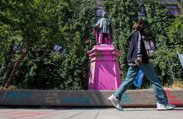 A person walks past Ryerson statue covered in paint.