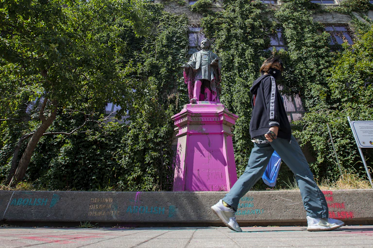 A person walks past Ryerson statue covered in paint.