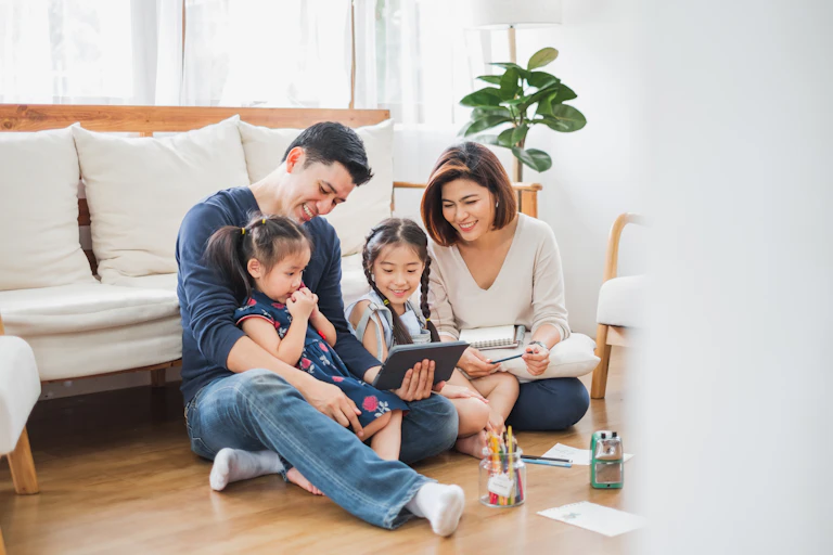 Migrant parents reading on a tablet with two young daughters.