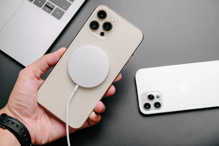 A hand holds an iPhone 12 attached to a charger.