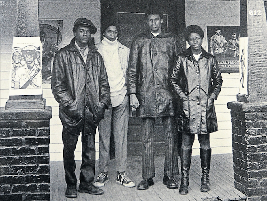 Four members of the Black Panther Party stand outside a house that served as the group's headquarters