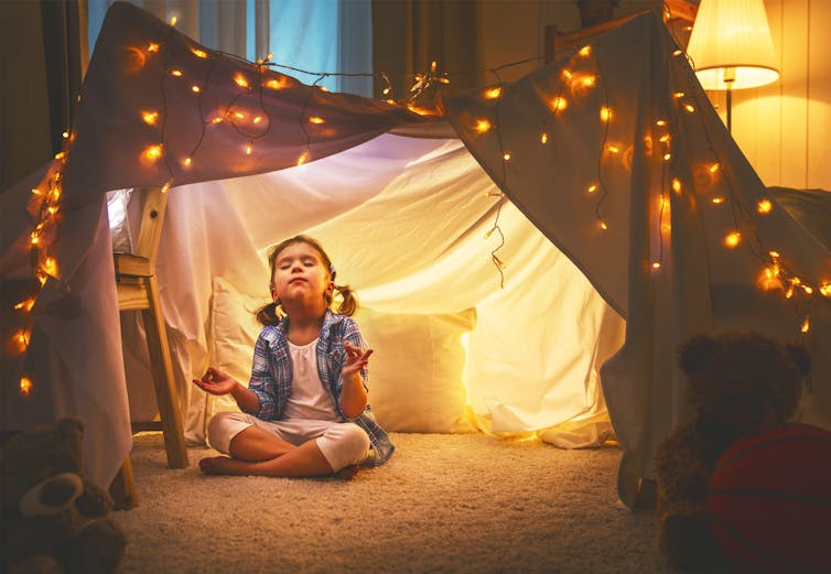 A girl meditates under a sheet covered in lights