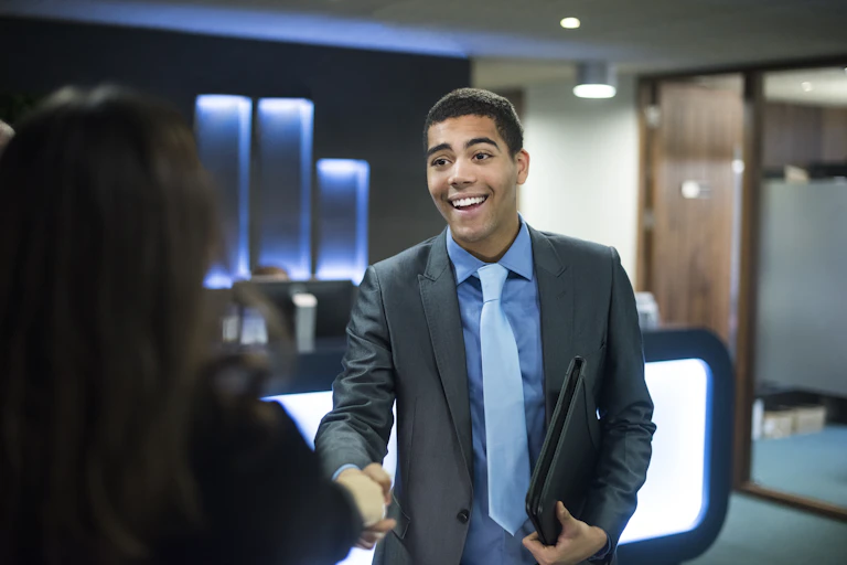 A young African American male shakes hands with a colleague on his first day of work.