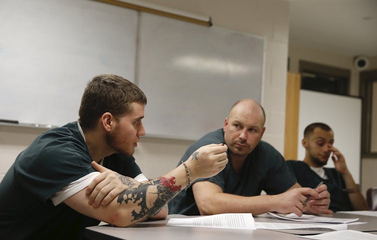 Male prisoners sit at a desk and talk about recovery.