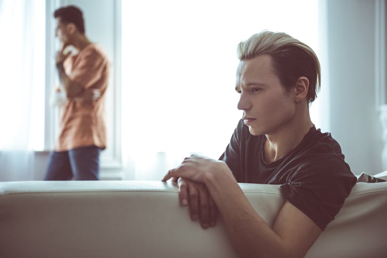 A young man looks serious while an older relative stands in the background.