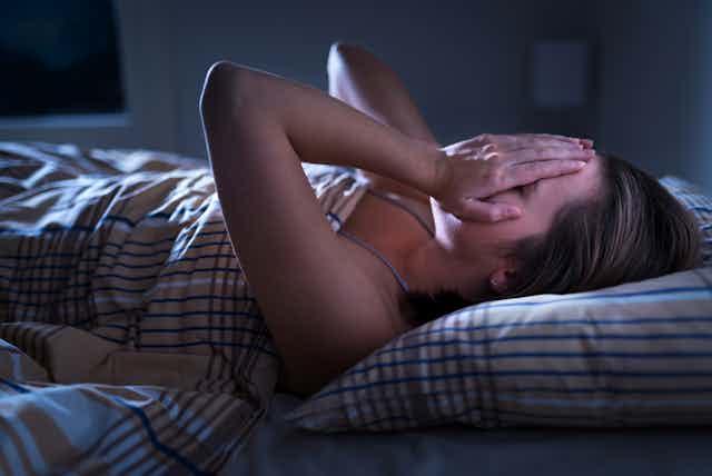 A woman lies in bed with her hands over her face.